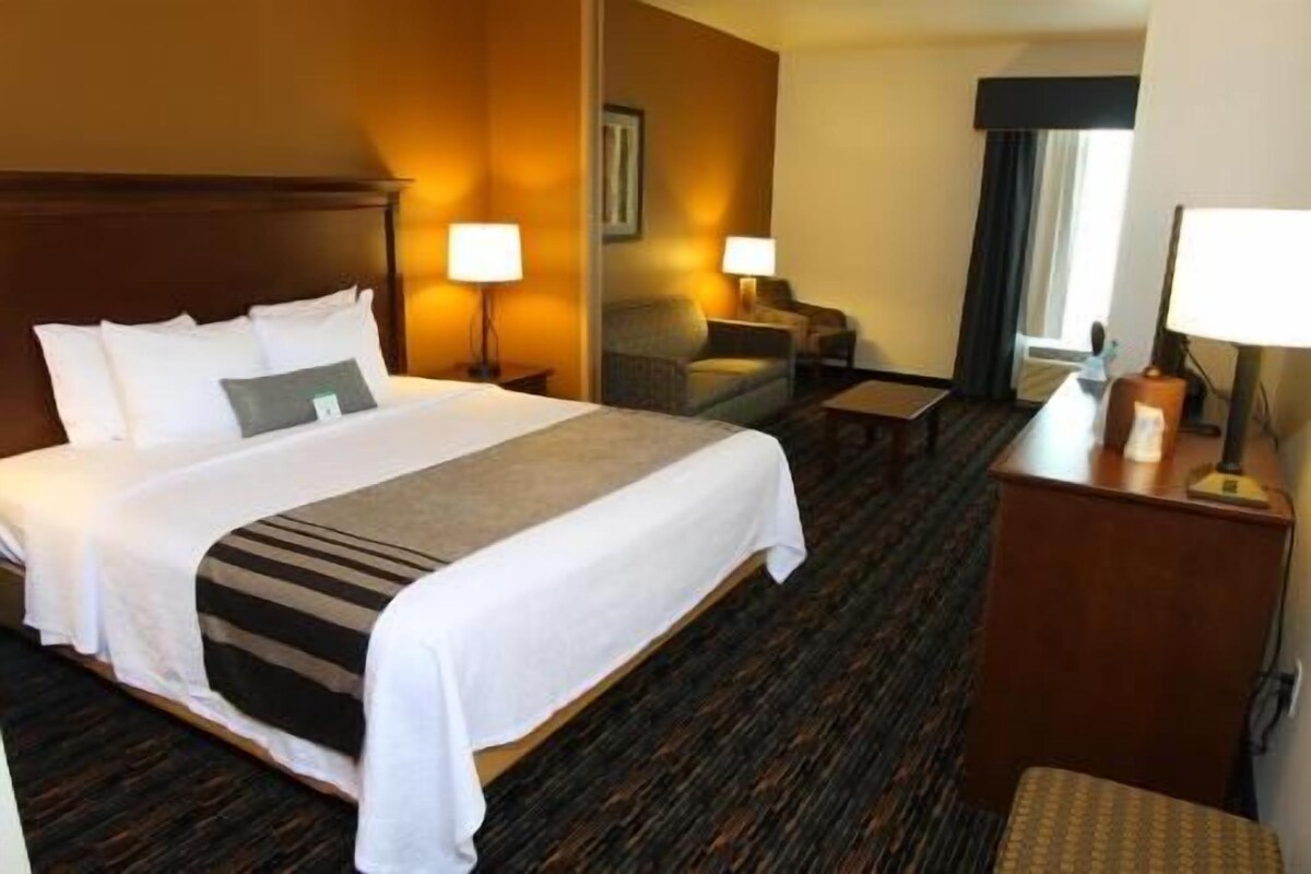 A hotel room with a large bed, two bedside tables, a desk, a chair, and a lamp.