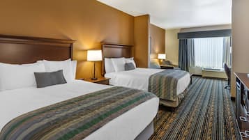 Habitación de hotel con dos camas, un ventanal con cortinas, un escritorio y piso alfombrado.