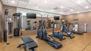 Een sportschool met diverse trainingsapparaten, een spiegelwand en een bank.