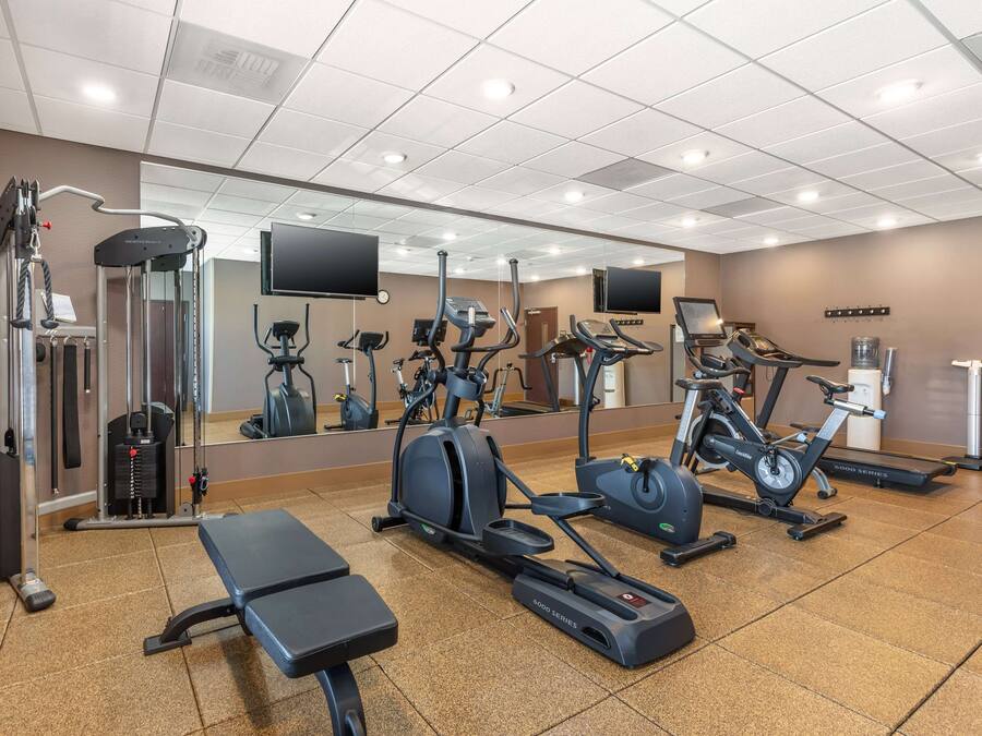 A gym with various exercise equipment, a mirrored wall, and a bench.