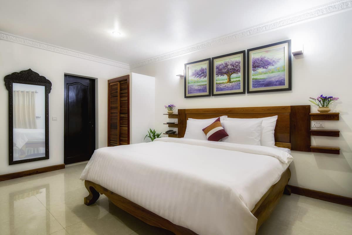Un dormitorio ordenado con una cama grande, un cabecero de madera y dos cuadros enmarcados en la pared.