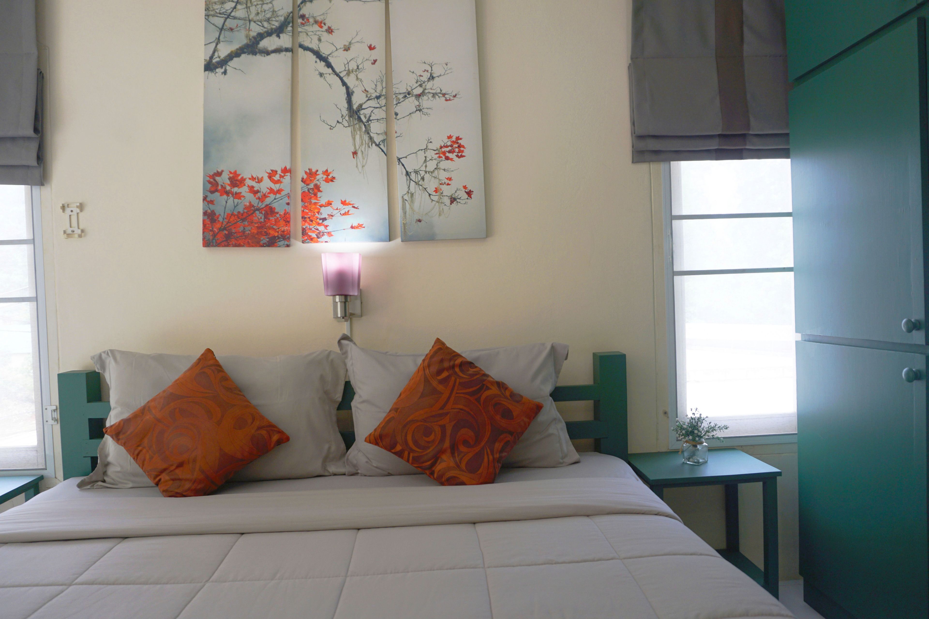 A bed with two pillows, a wall-mounted lamp, and a painting above it.