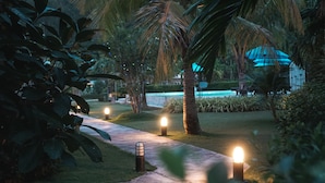 Un camino bordeado de palmeras e iluminado por pilares, que conduce a una zona de piscina.