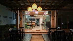 Un espacio al aire libre para comer con mesas y sillas de madera, un camino central y faroles colgantes.