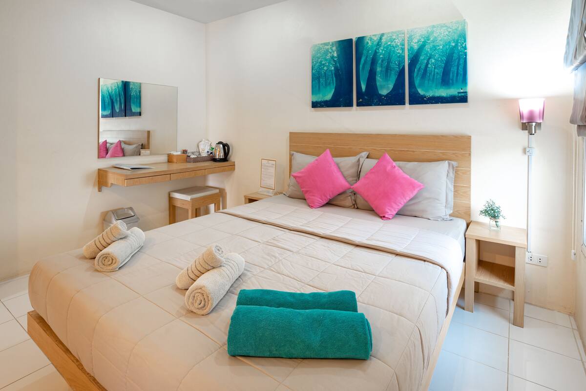 A bedroom with a large bed, two pillows, a bedside table, a nightstand, a mirror, and artwork on the wall.