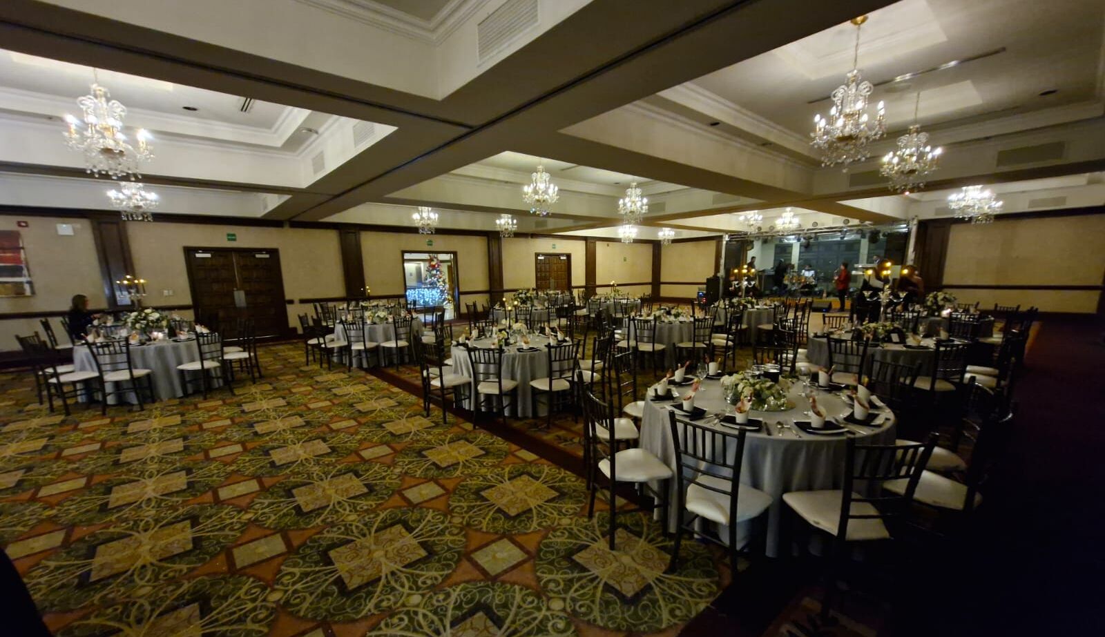 A banquet hall with round tables, chandeliers, and a patterned carpet.