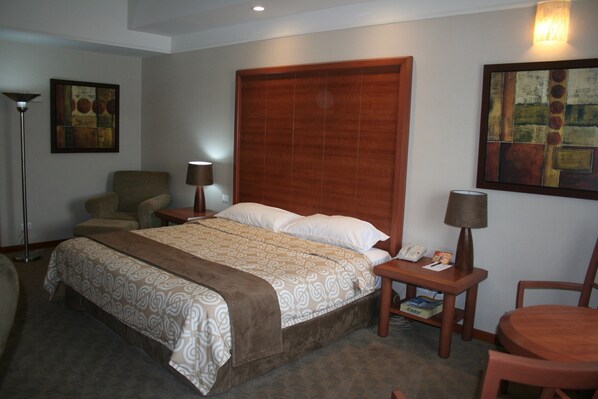 A hotel room with a large bed, a chair, a desk with a lamp, and artwork on the walls. - Hotel Royal Palace (Hermosillo)