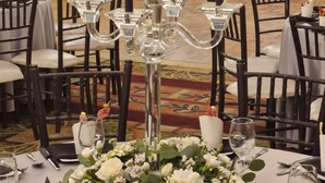 Un ambiente formal para cenar, con candelabro como centro de mesa, manteles blancos y sillas negras.