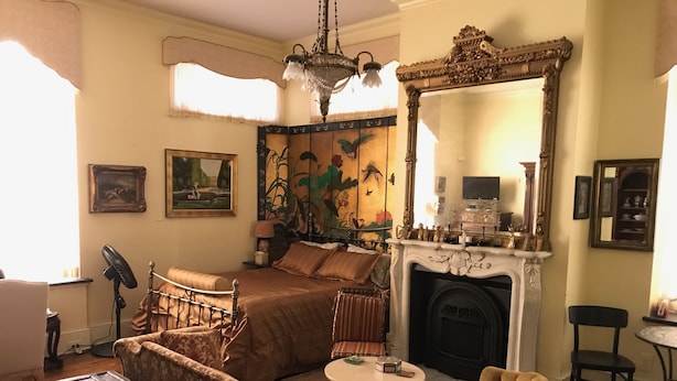 A traditional room with a bed, a fireplace, a mirror, and a fan. - Trade Winds Bed and Breakfast (Philadelphia)
