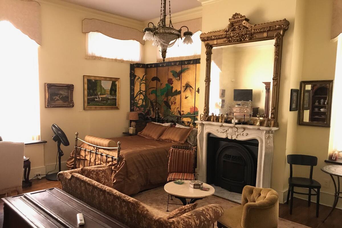 A traditional room with a bed, a fireplace, a mirror, and a fan.