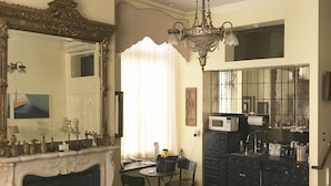 A living room with a fireplace, a chandelier, a dining area, and a kitchen with a microwave. - Trade Winds Bed and Breakfast (Philadelphia)