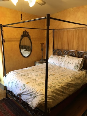 A four-poster bed with floral bedding, a round mirror, and a bedside table with a vase. - Trade Winds Bed and Breakfast (Philadelphia)
