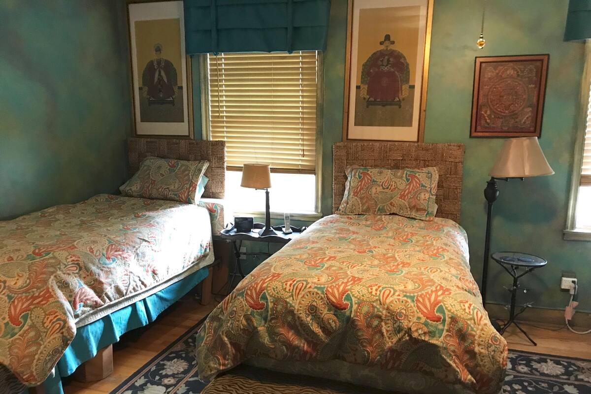 A room with two beds, a small table, a lamp, and framed artwork on the walls.