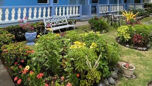 A two-story building with a blue exterior, white balconies, and a garden area with various plants and a bench. - Skyblue Beach Apartments (Villa)