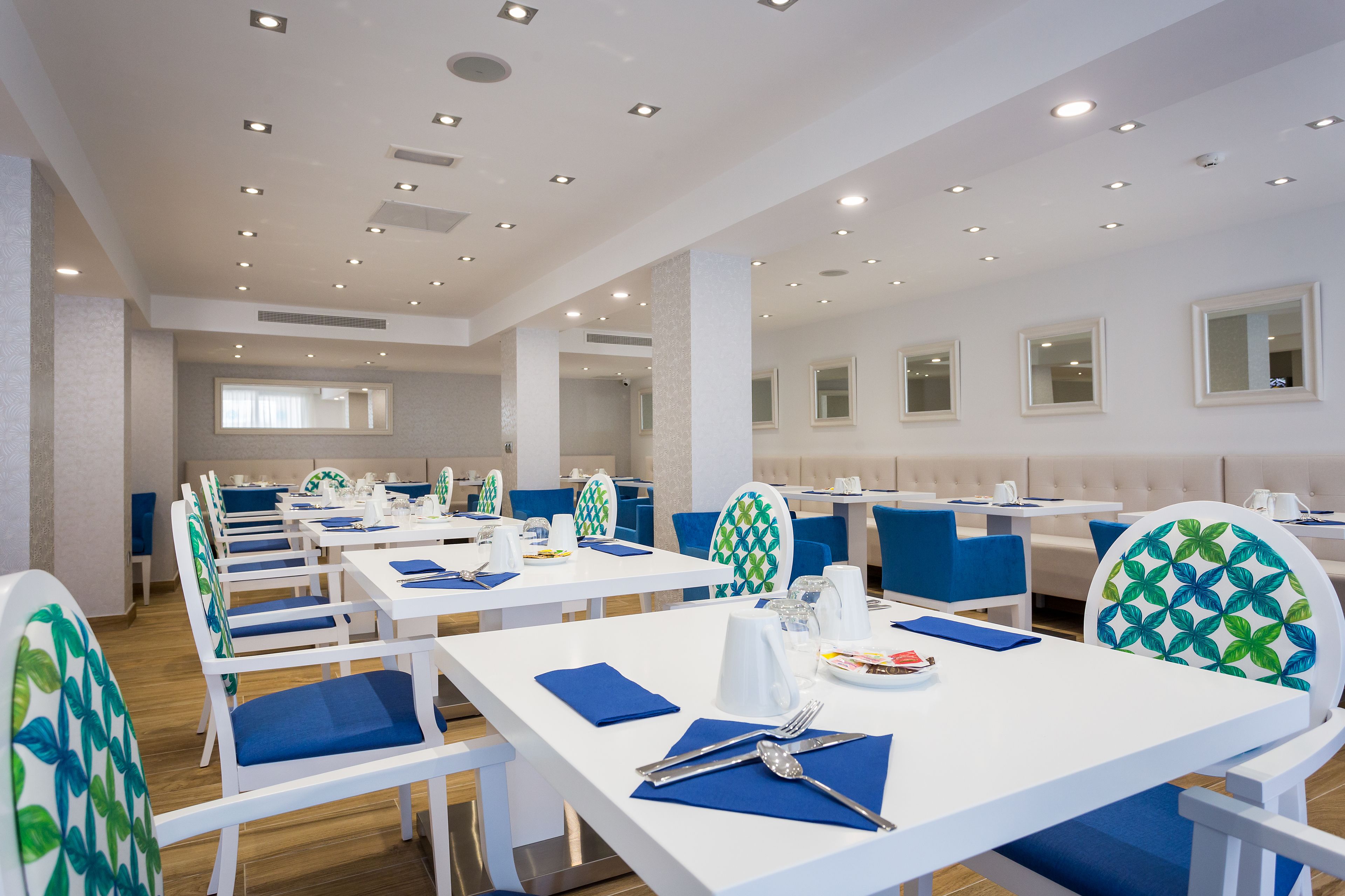 Un comedor amplio con mesas blancas y sillas azules, que ofrece diversas opciones de disposición de los asientos y un diseño de techo moderno.
