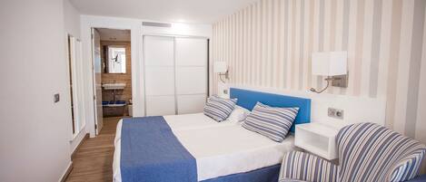 Habitación de hotel con cama, una silla, mesita de noche, espejo y baño visible a través de una puerta abierta.