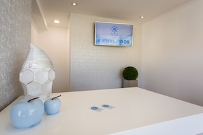 Welcome to our reception area, featuring a large wall panel, flat-screen TV, and modern reception desk.