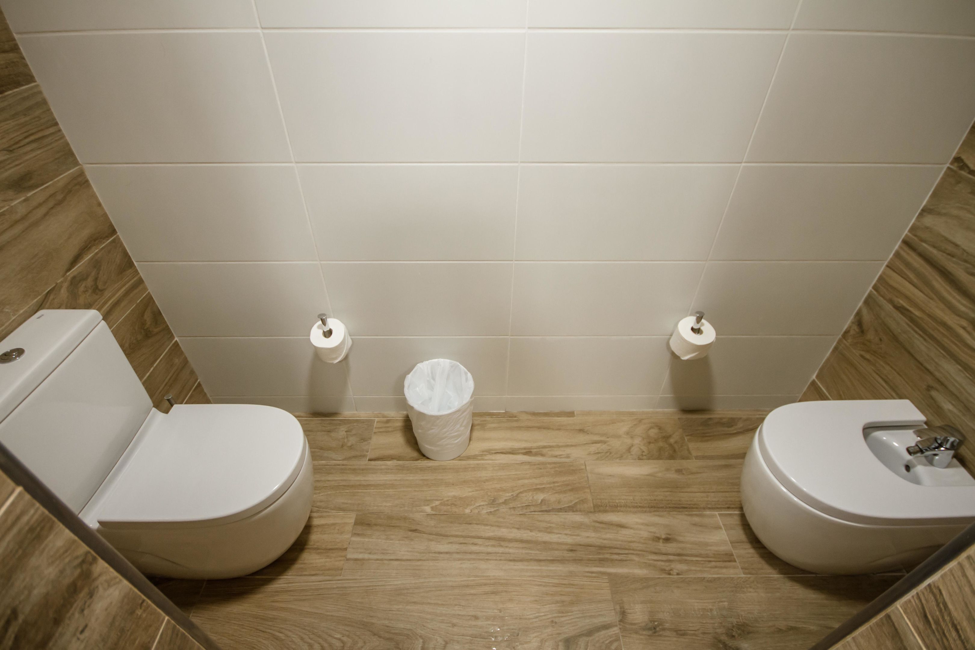 Un baño moderno con dos inodoros, un cubo de basura y un dispensador de papel higiénico en la pared.