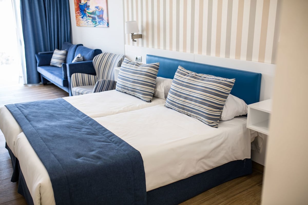 A hotel room with a bed, a sofa, a nightstand, and a wall with vertical stripes.