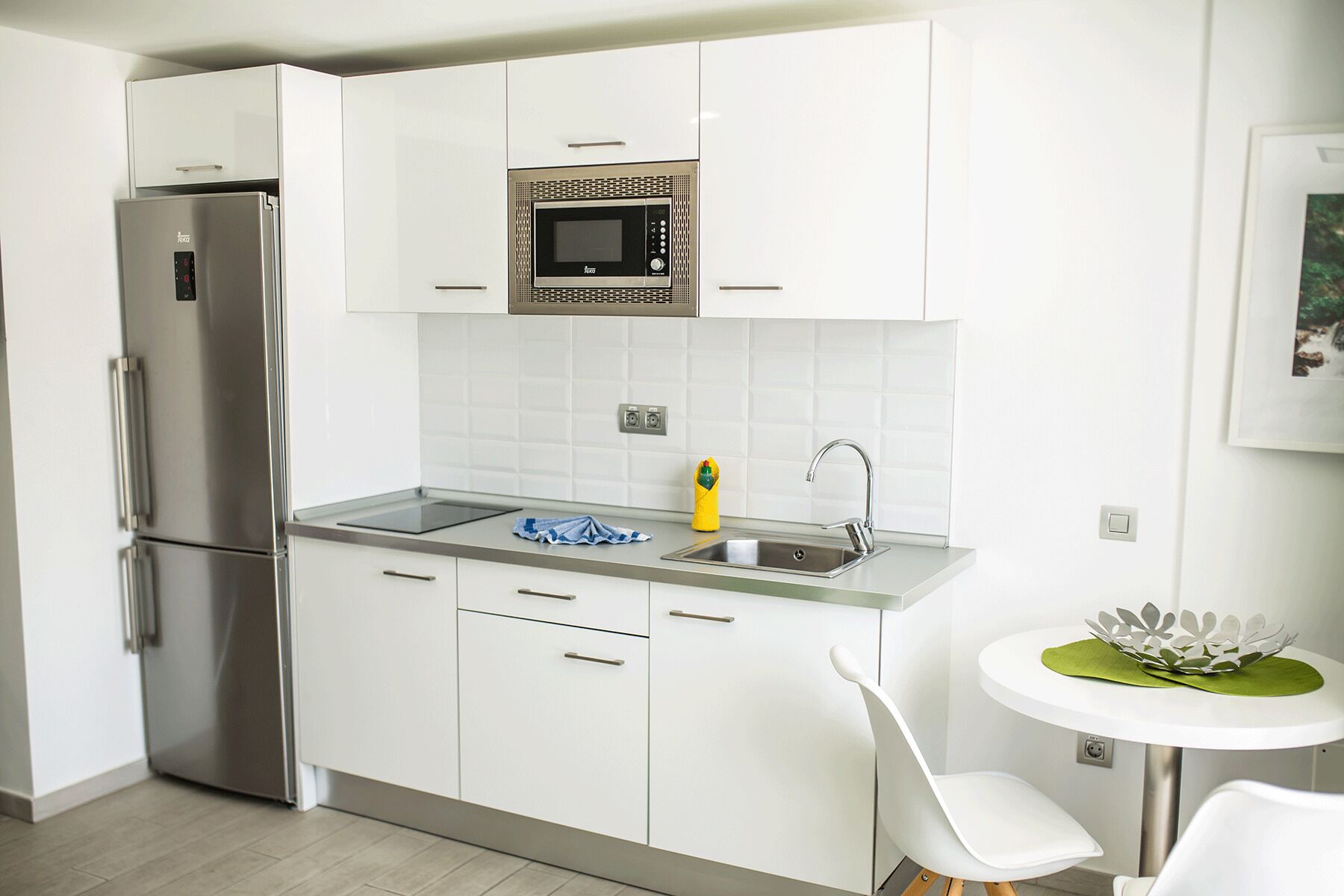 Una cucina moderna con mobili bianchi, un frigorifero in acciaio inossidabile, un forno a microonde e un lavello.
