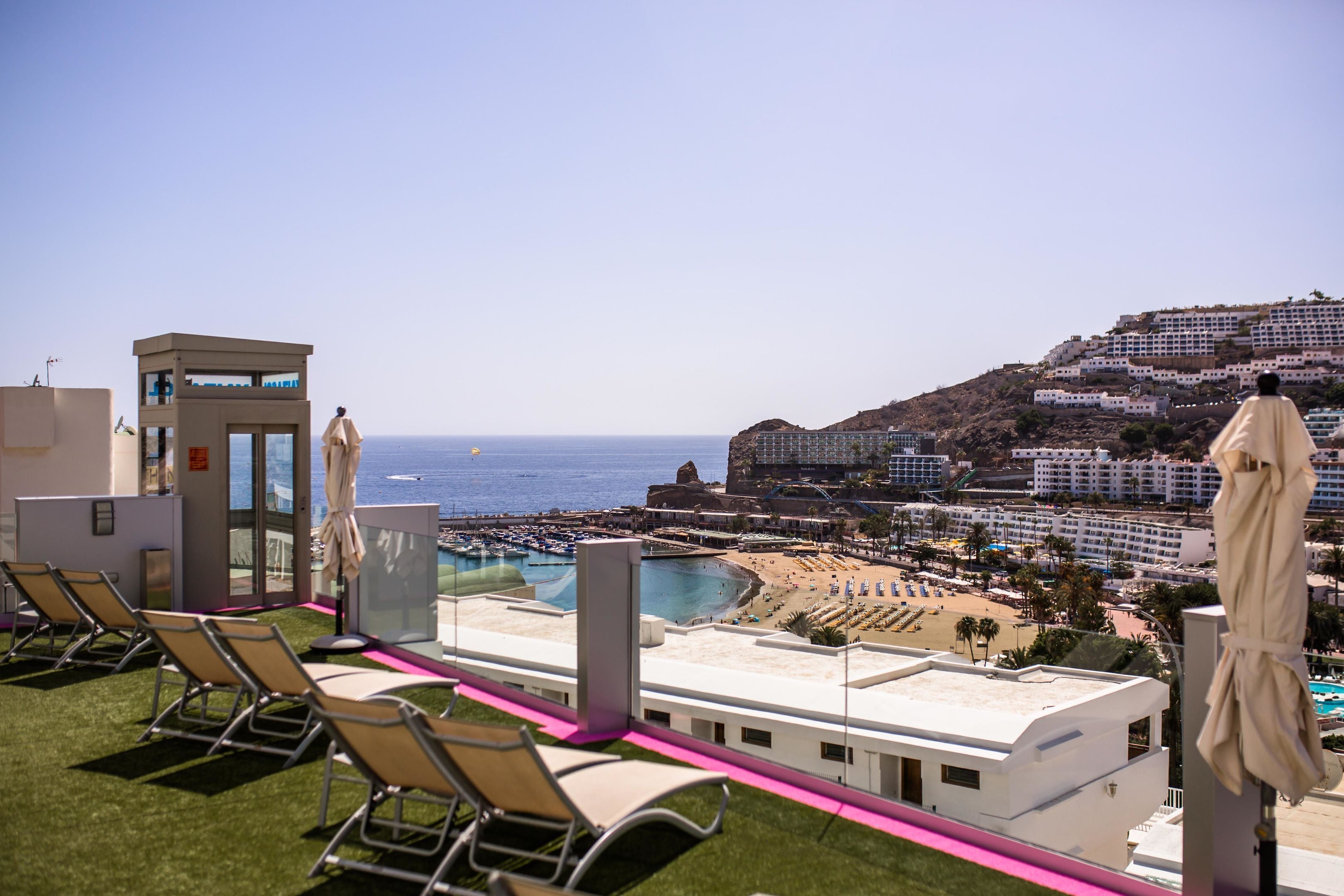 A rooftop terrace with lounge chairs, a pool, and a view of the beach and ocean.