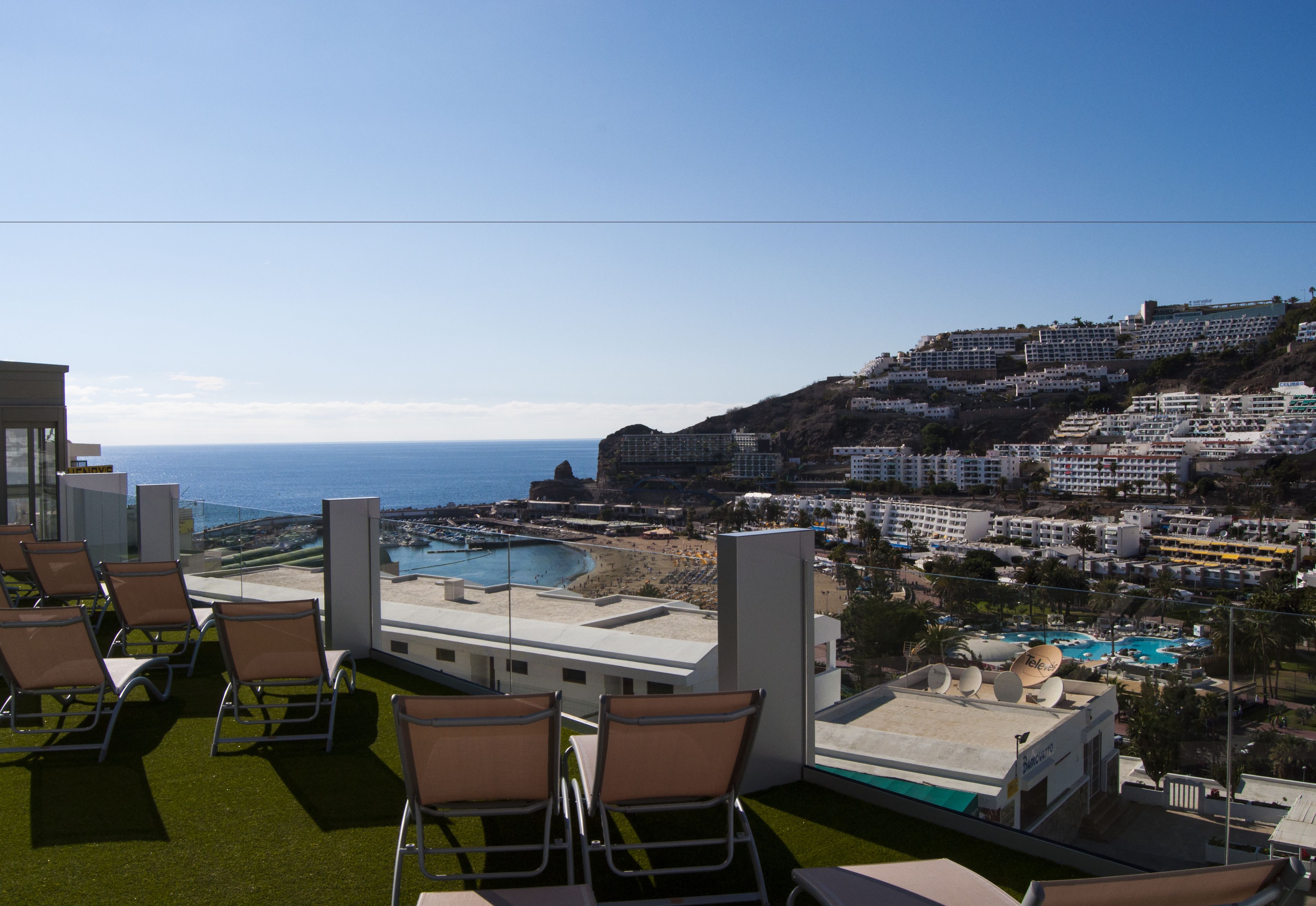 Terraza en la azotea con mobiliario exterior y vistas a una zona turística costera.