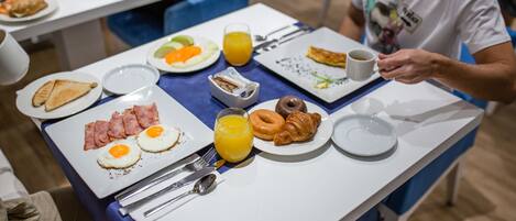 A breakfast setting with plates of eggs, bacon, toast, croissants, and orange juice.
