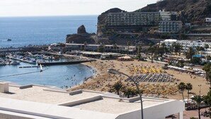 Ein Hotel an der Küste mit Blick auf den Strand, mehreren Balkonen und einem Yachthafen mit Booten.