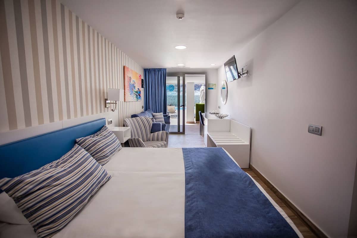 A hotel room with a bed, a sofa, a desk, and a view of the city through a window.