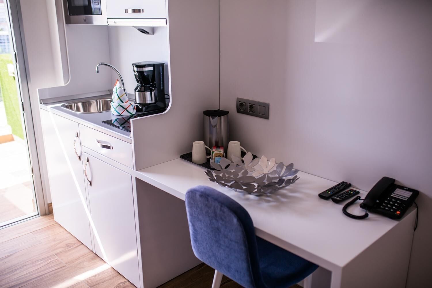 A compact kitchenette with a coffee maker, a kettle, and a microwave. There is a small table with a decorative bowl and a telephone.