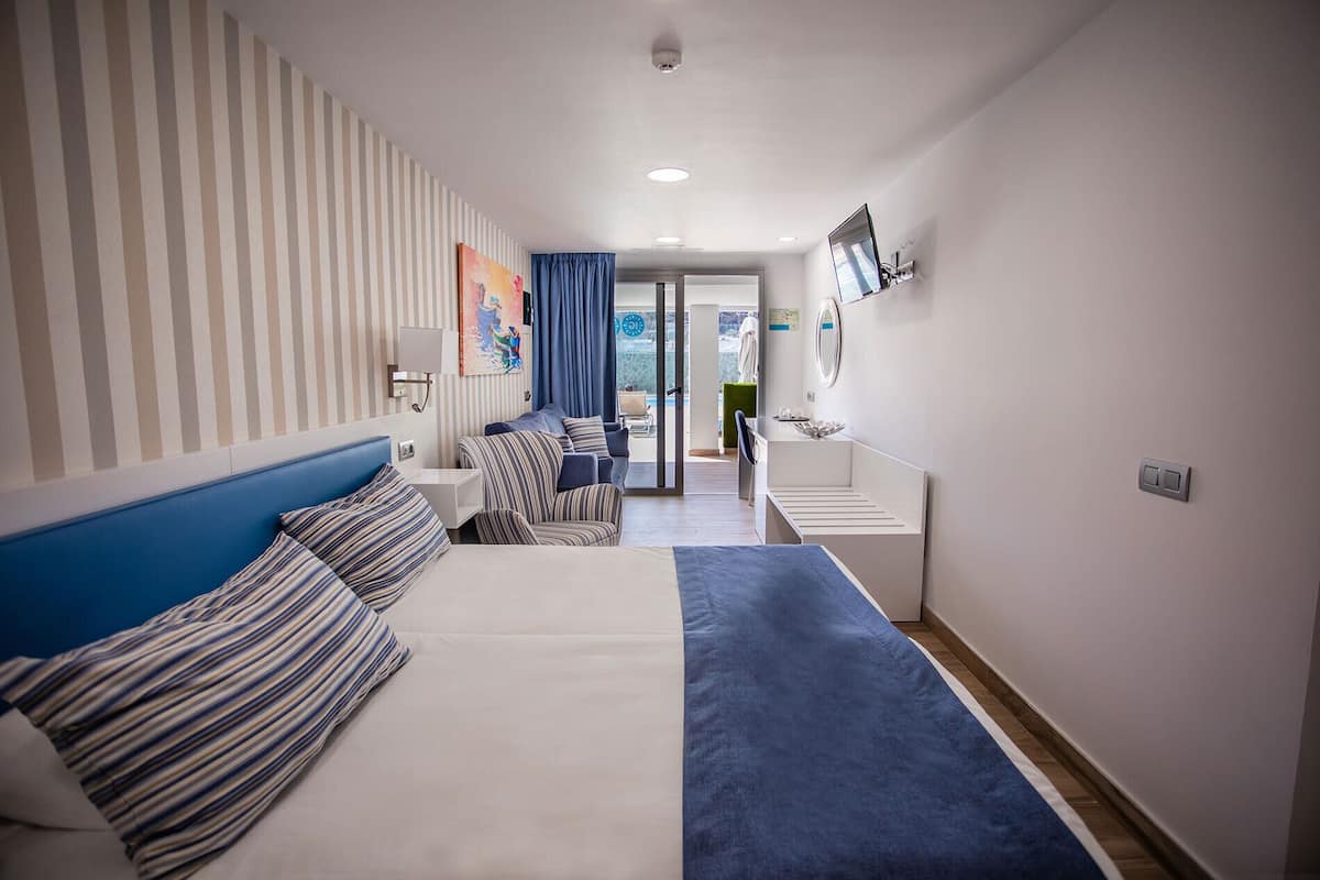 A hotel room with a bed, a seating area with a sofa and armchairs, a small table, and a bathroom with a mirror and sink.