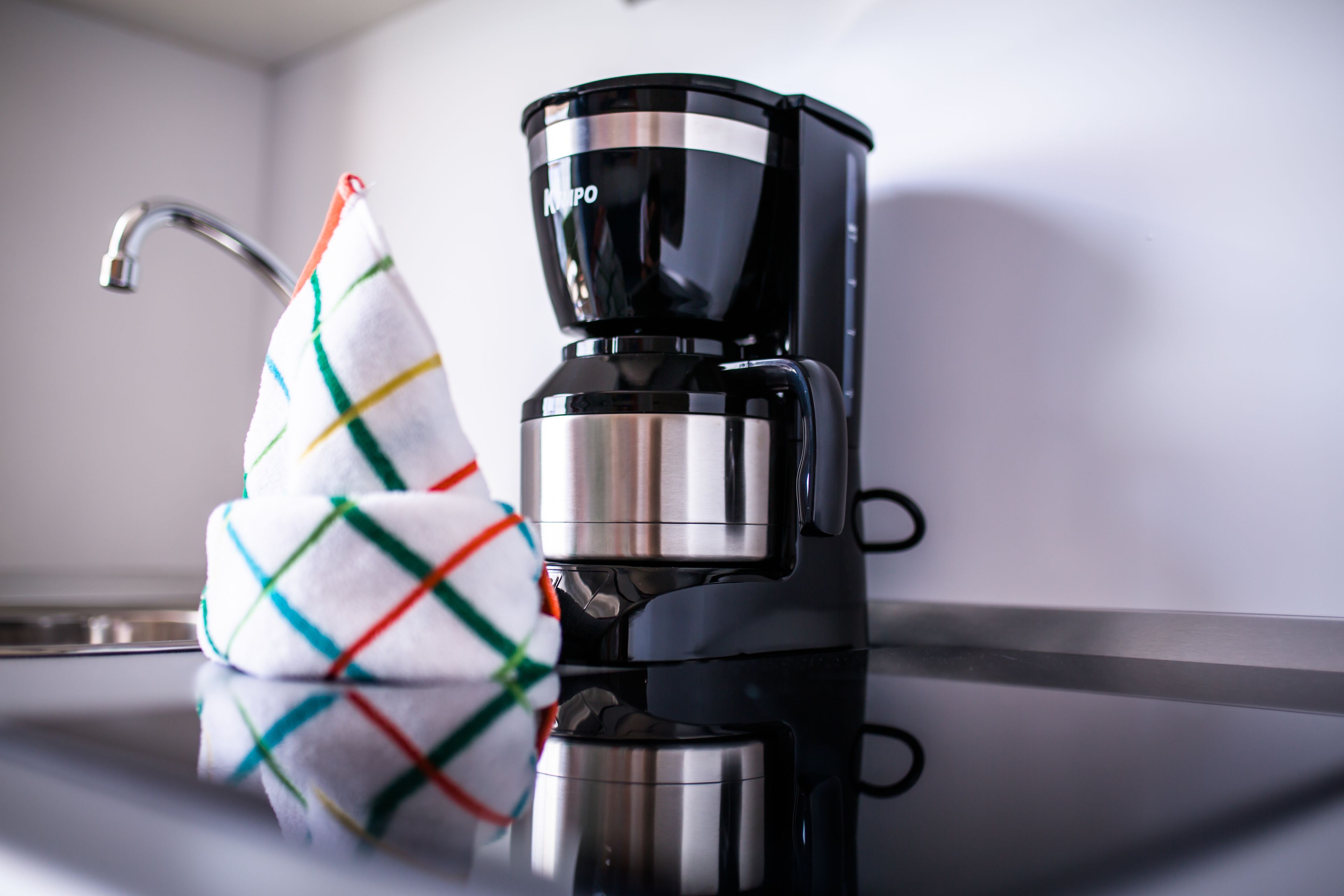 A black coffee maker on a kitchen counter with a colorful kitchen towel hanging on the faucet.