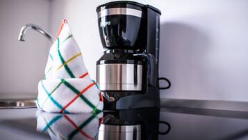A black coffee maker on a kitchen counter with a colorful kitchen towel hanging on the faucet.