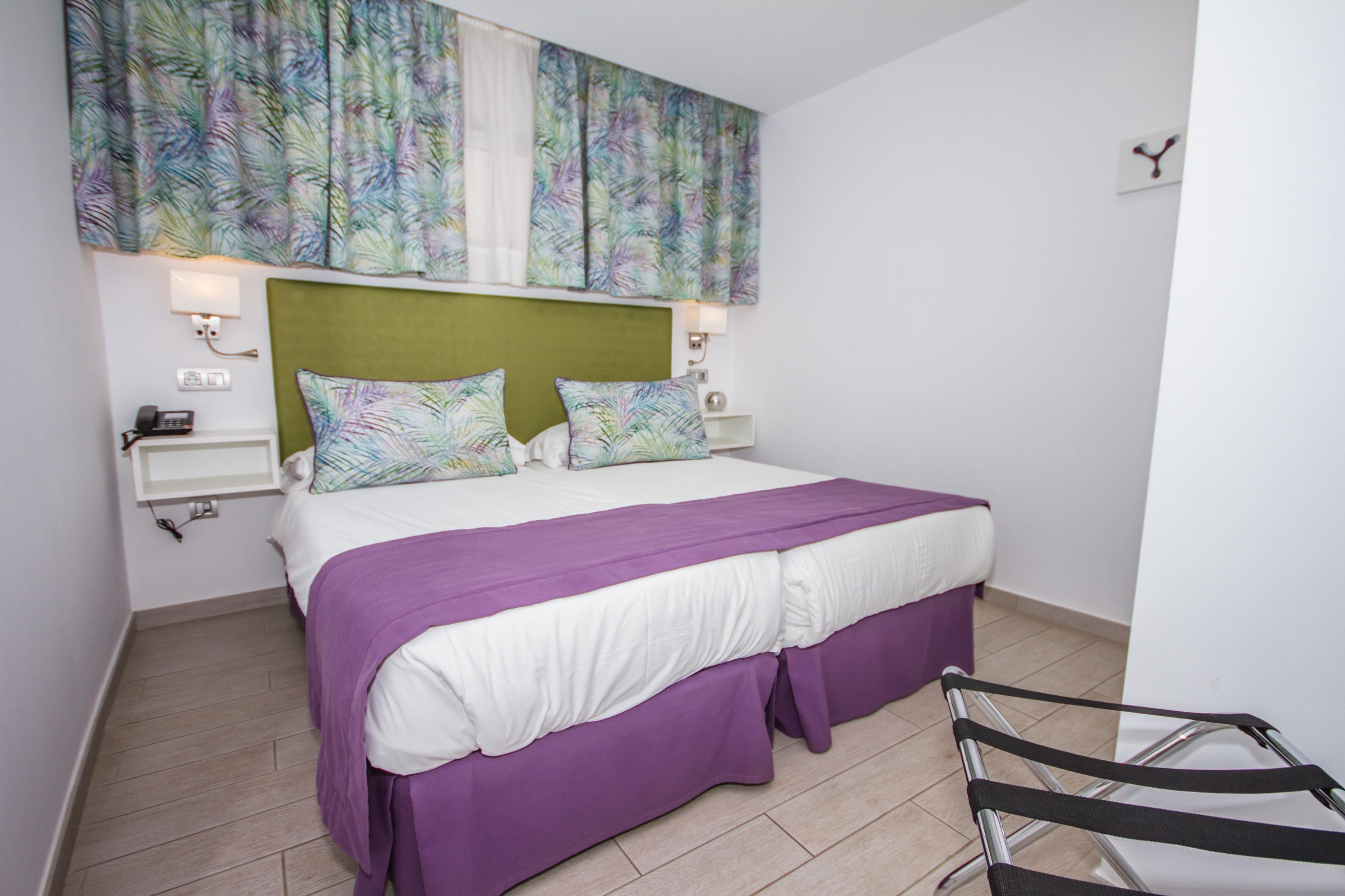 A bedroom with a large bed, green headboard, white and purple bedding, and a wall-mounted artwork.