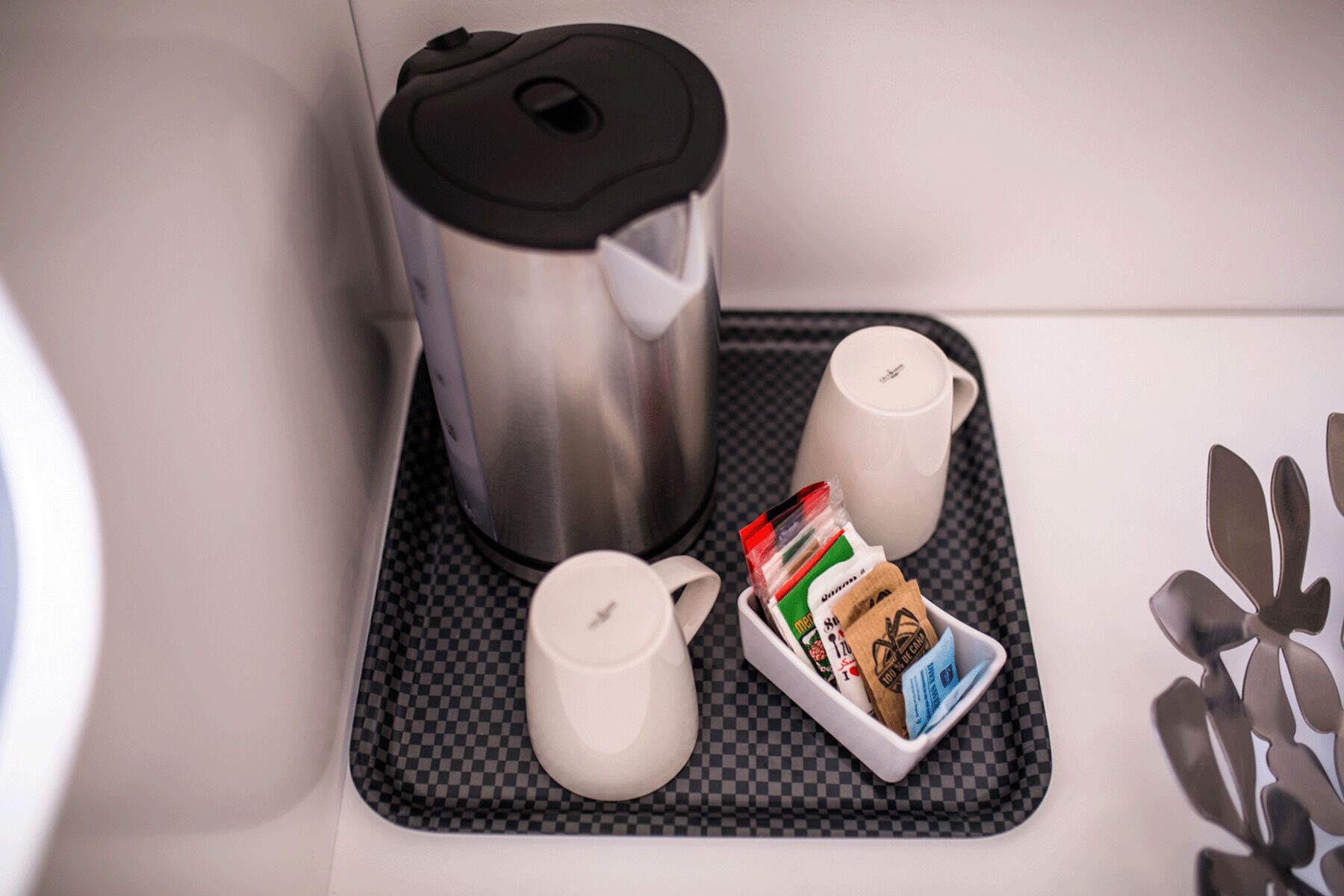 A kitchen area with a coffee maker, two cups, a tray with coffee pods, and a kettle.