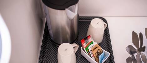 Una cocina con cafetera, dos tazas, una bandeja con cápsulas de café y un hervidor.