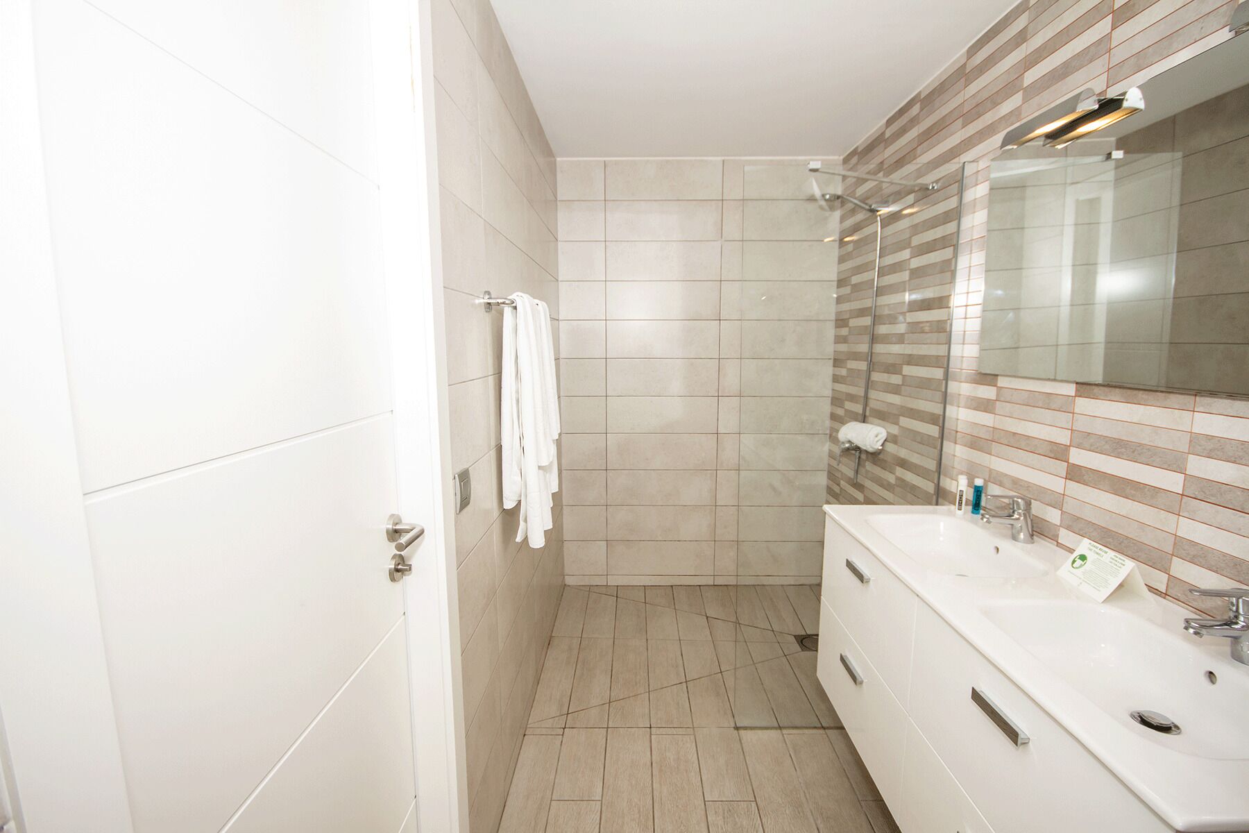 Une salle de bain moderne avec un grand miroir, un meuble-lavabo blanc et un espace douche.