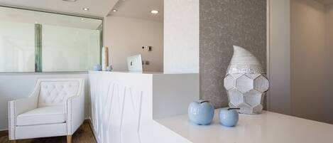 A reception area with a white reception desk, a tufted white chair, and a decorative wall piece.