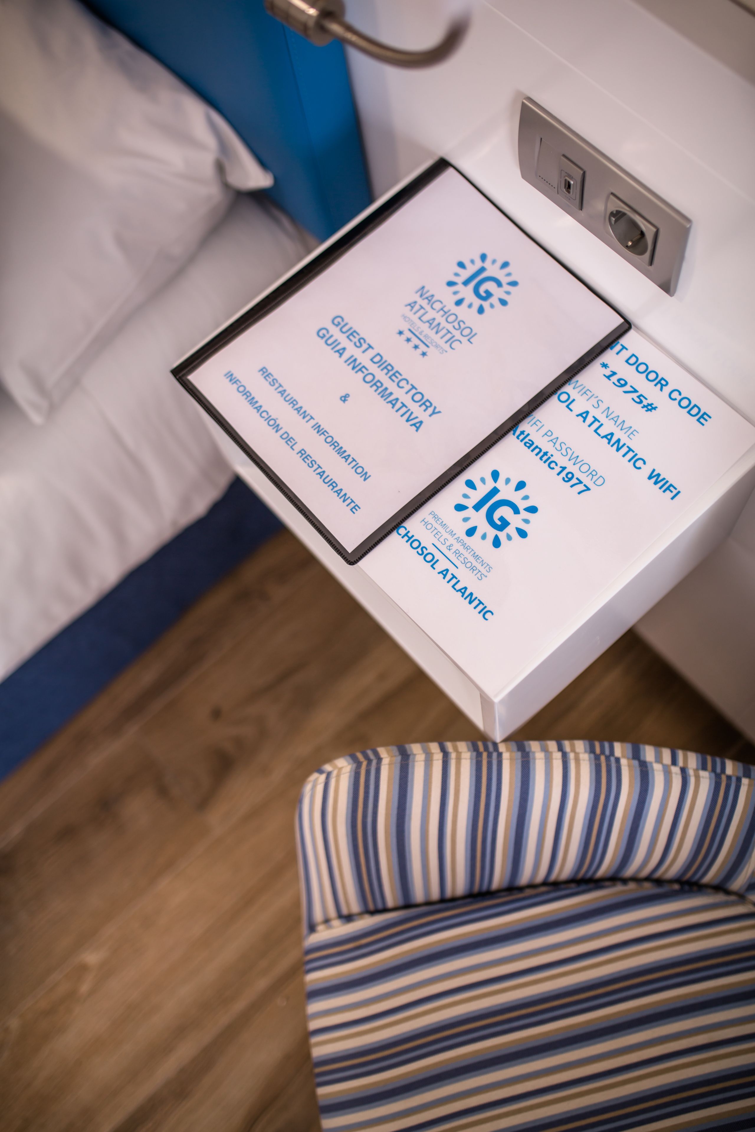Hotellihuone, jossa on sänky, yöpöytä, jossa on kyltti, ja raidallinen tuoli.