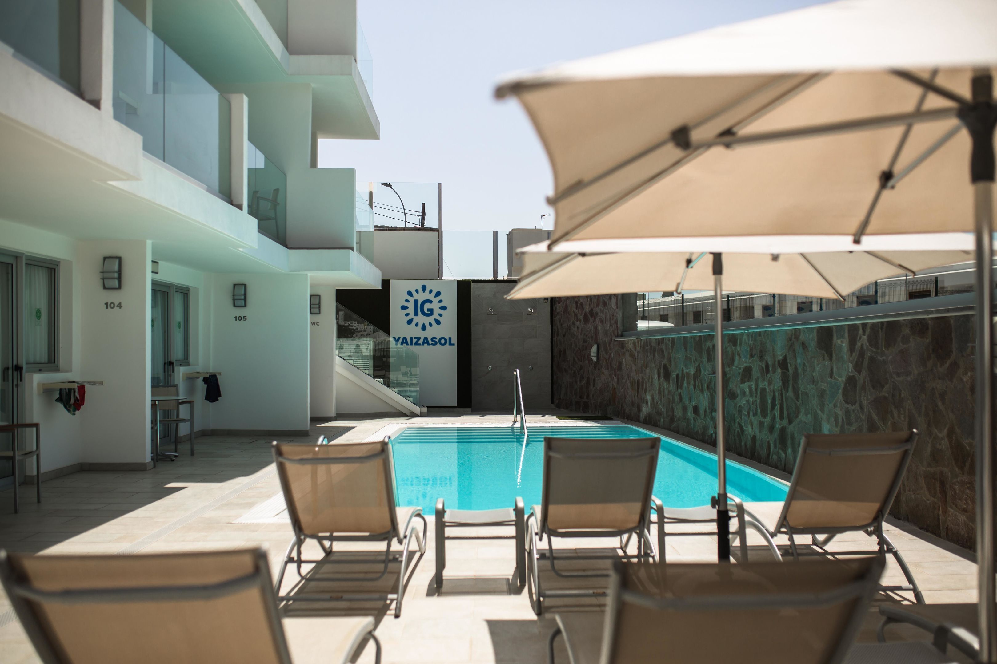 Zona de piscina con sillones de descanso y un cartel que dice 'IG YAIZASOL'.