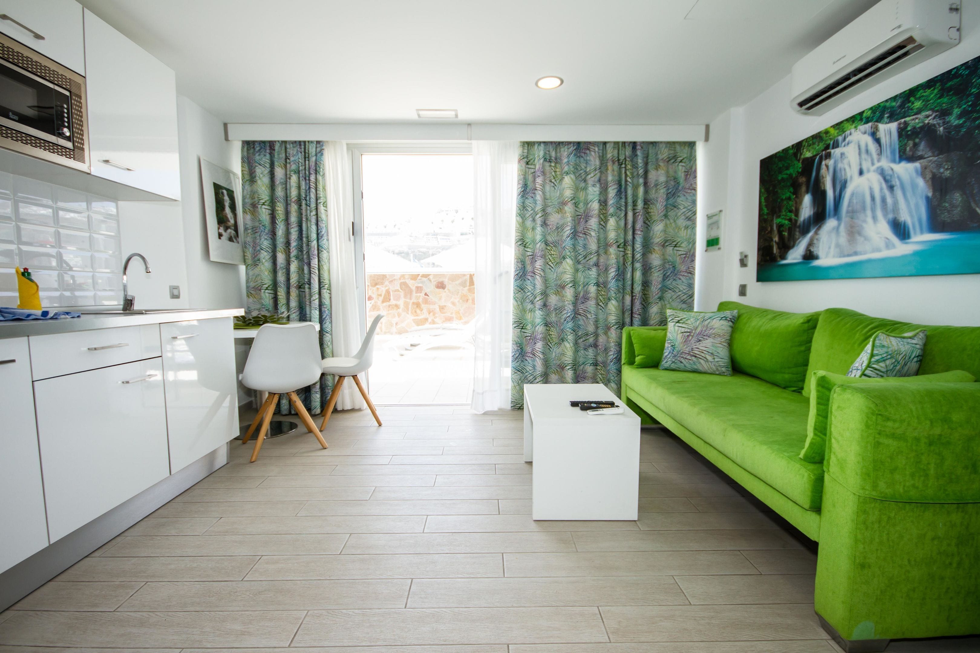 Una sala moderna con un sofá verde, una mesa de centro blanca y vistas a una cascada a través de una ventana.