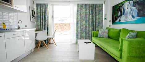 A modern living room with a green sofa, white coffee table, and a view of a waterfall through a window.