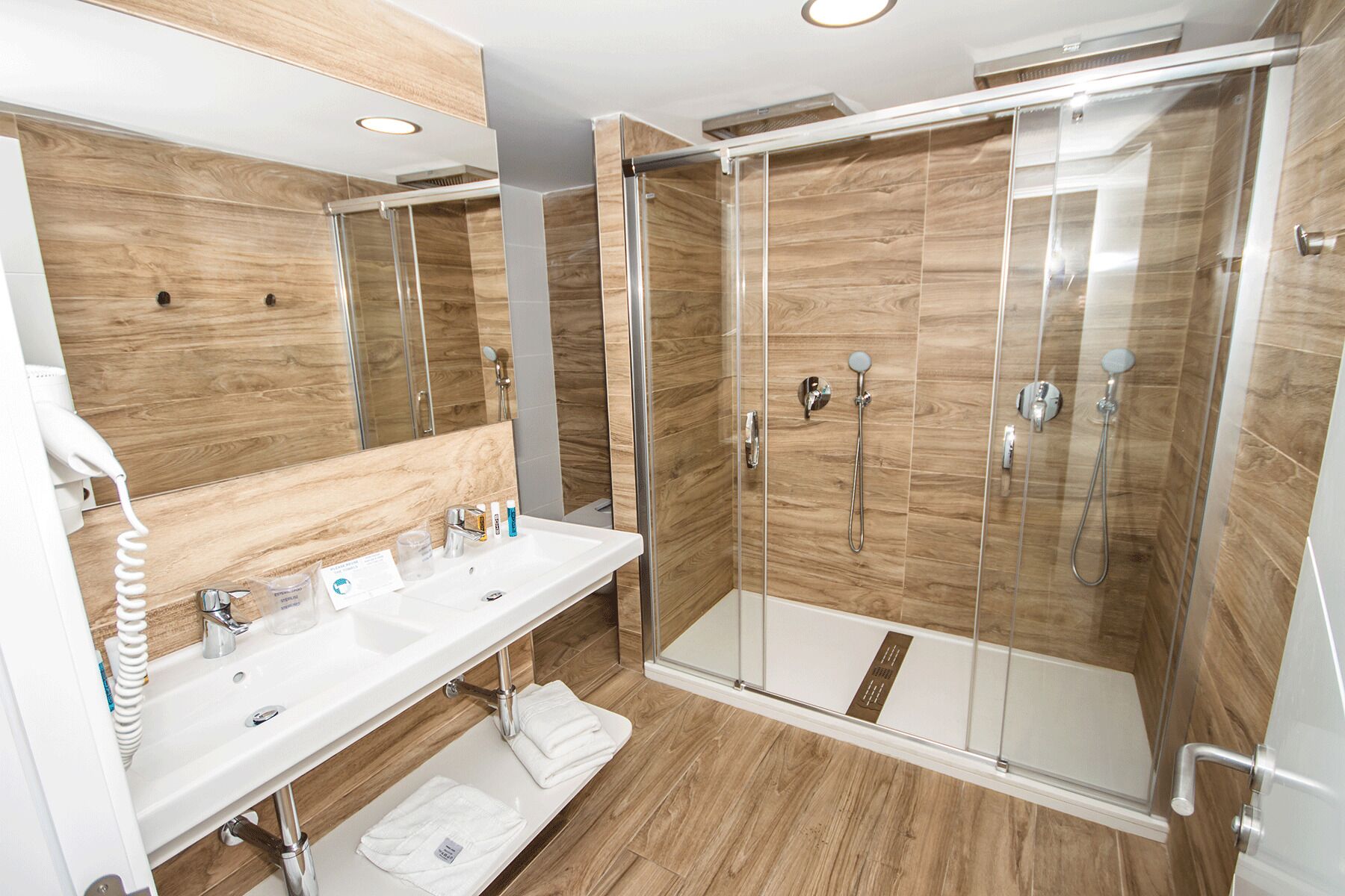A modern bathroom with a wooden floor, a white sink, a mirror, and a glass-enclosed shower area with a handheld showerhead.
