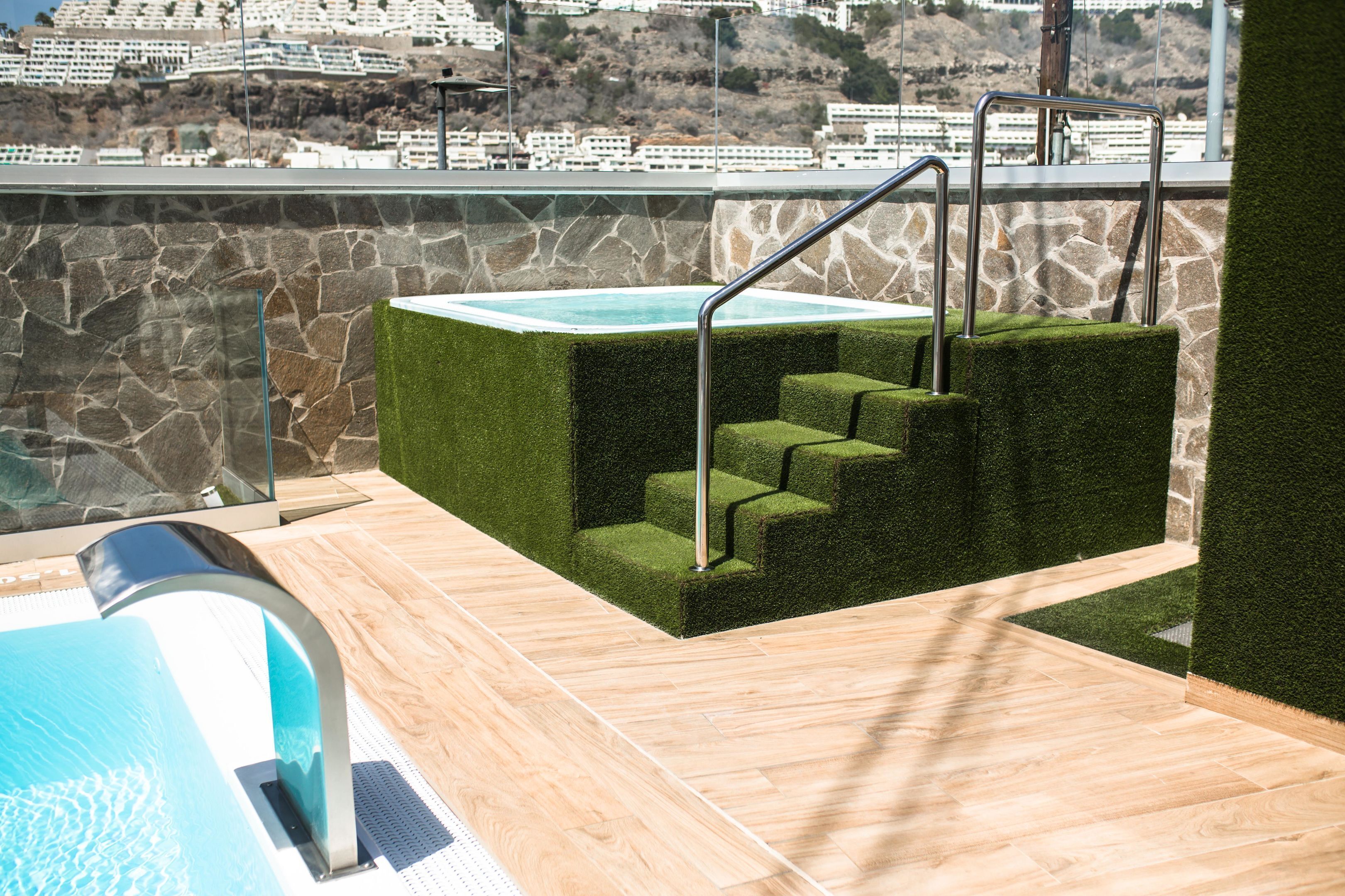 Una piscina al terrat amb una paret de pedra i escales cap a una terrassa.