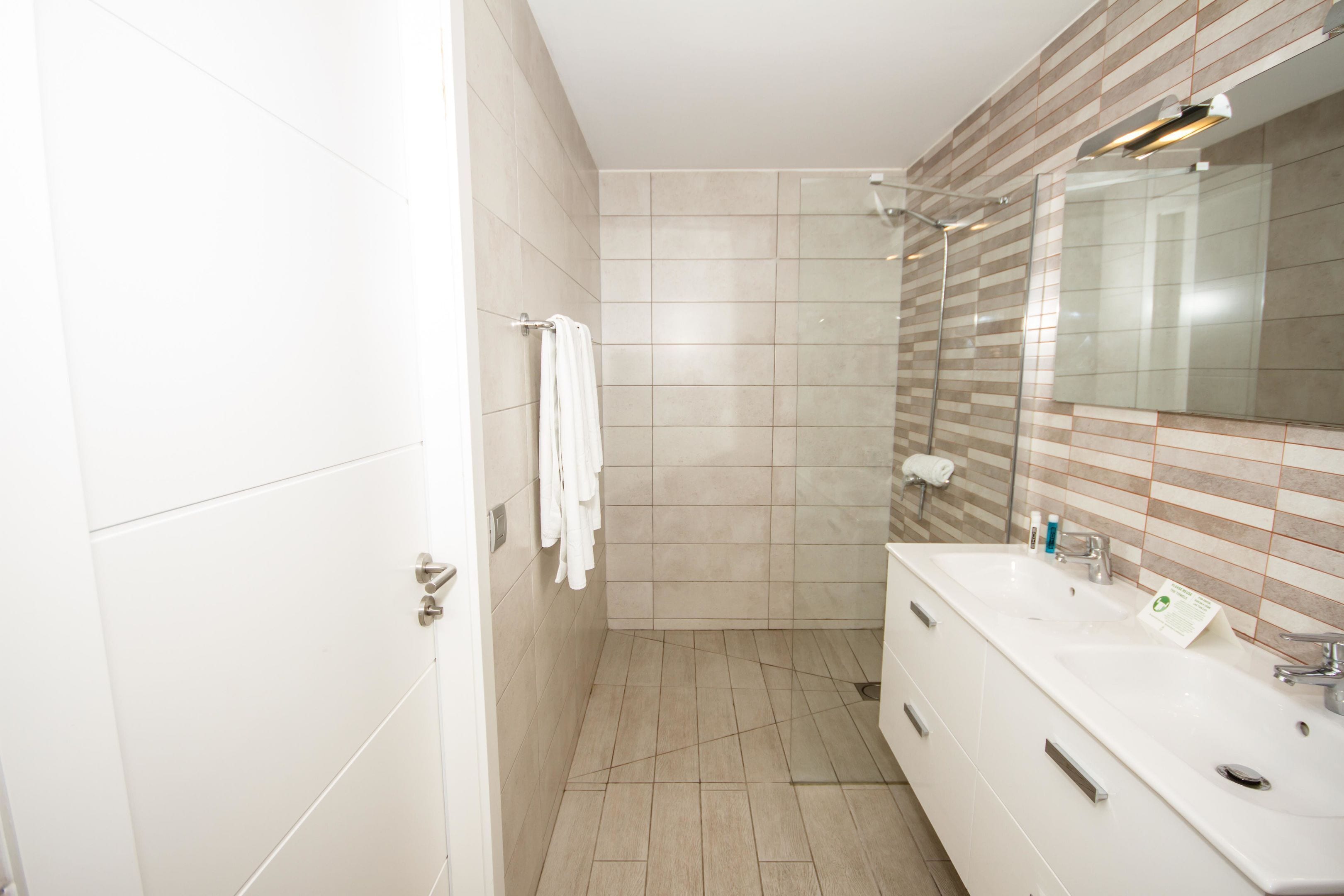 Un baño moderno con un espejo grande, tocador blanco y azulejos color beige.