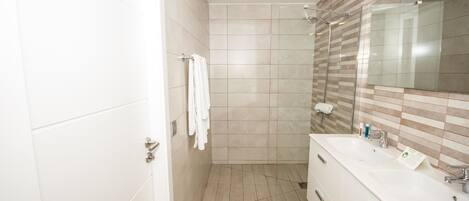 Un baño moderno con un espejo grande, tocador blanco y azulejos color beige.