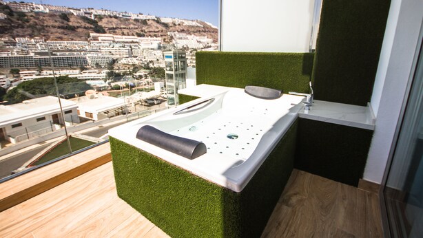 Ein modernes Badezimmer mit einem grünen Kunstgras-Akzent, einer weißen Arbeitsplatte und Blick auf eine Stadtlandschaft.