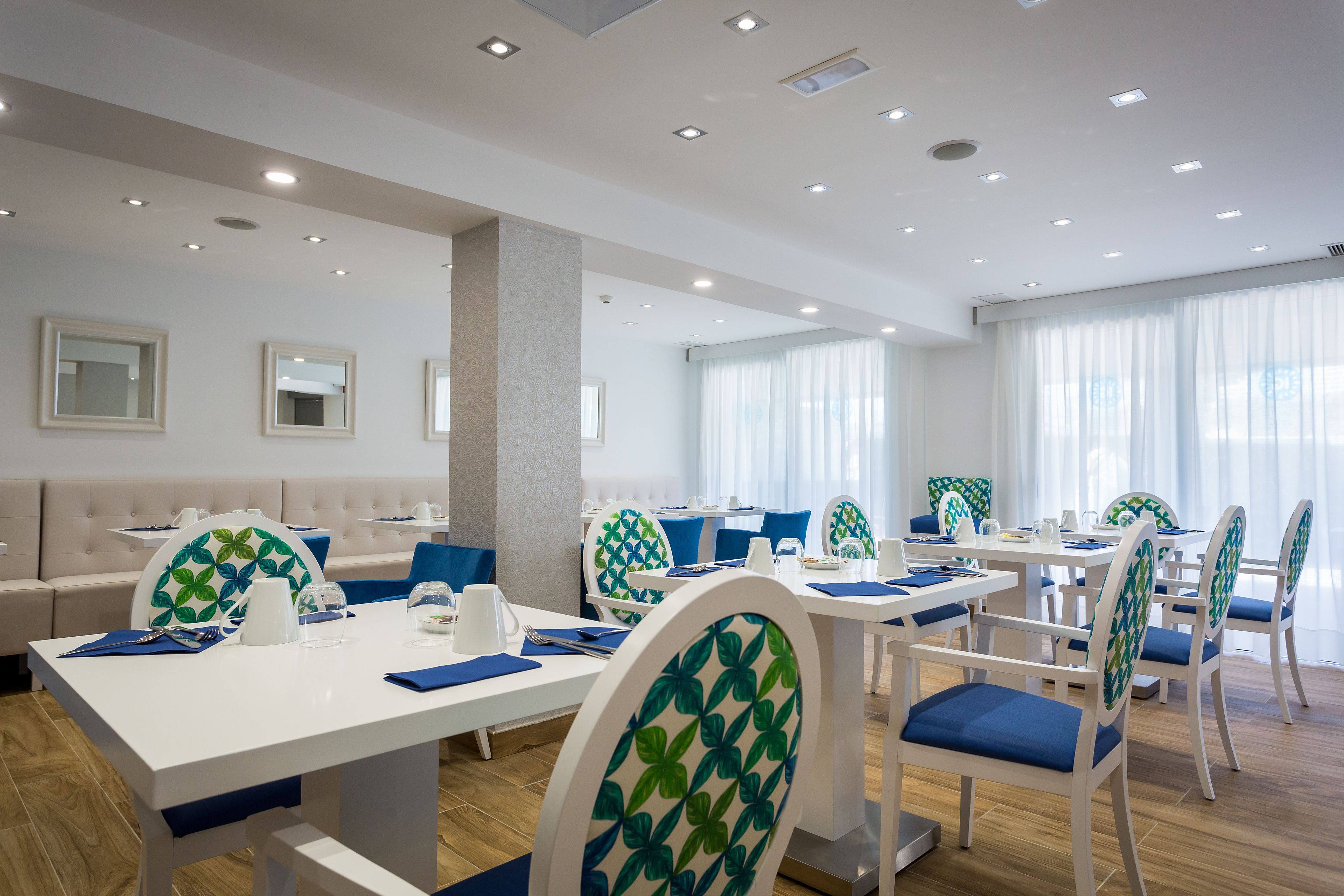 Un comedor moderno con mesas y sillas blancas, cojines azules y una paleta de colores neutros.