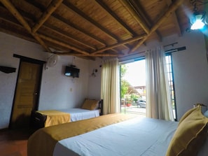 Una habitación con dos camas, techo de madera, televisión y ventana con cortinas.