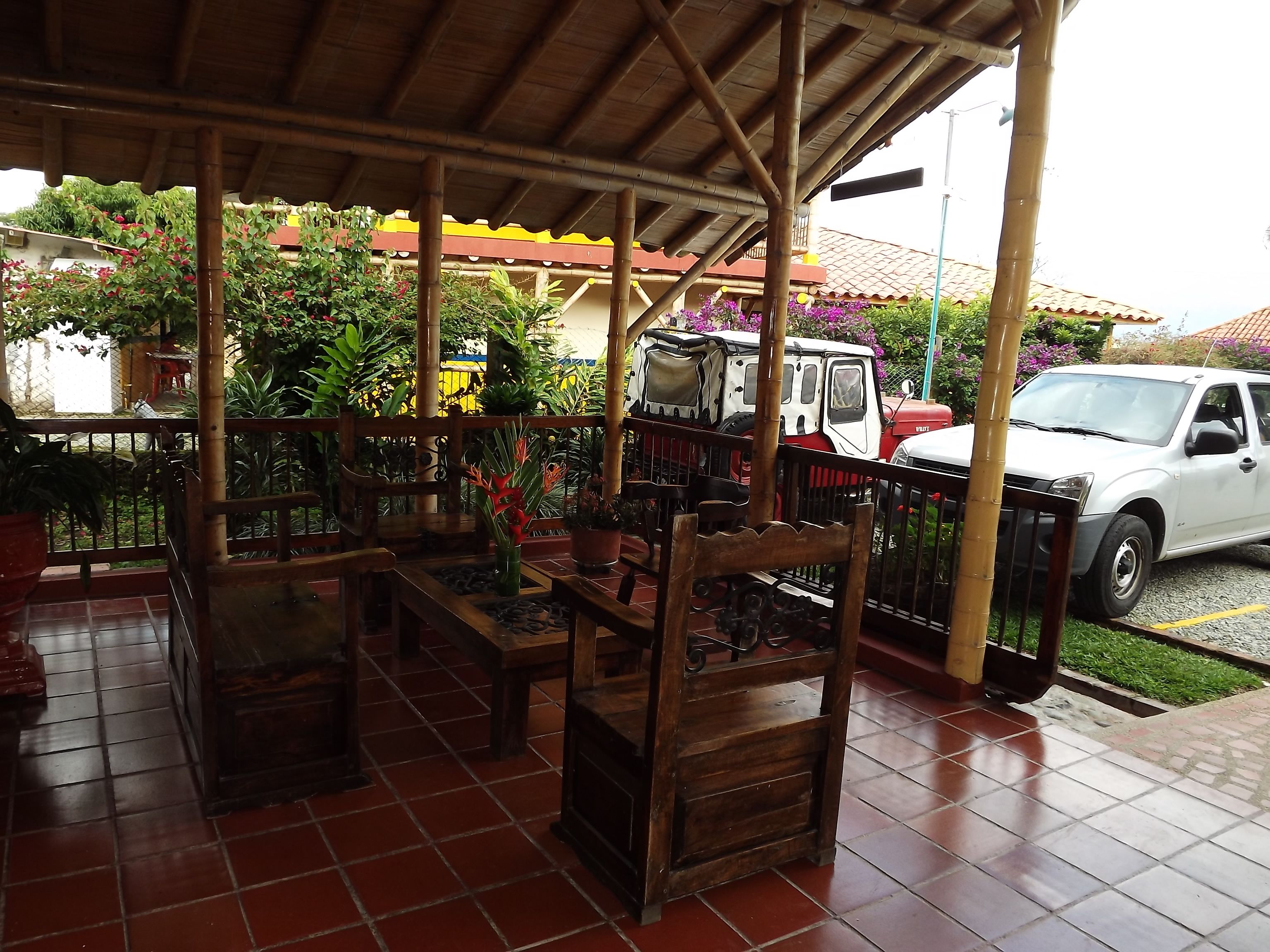 A covered outdoor area with wooden furniture and a white car parked nearby.